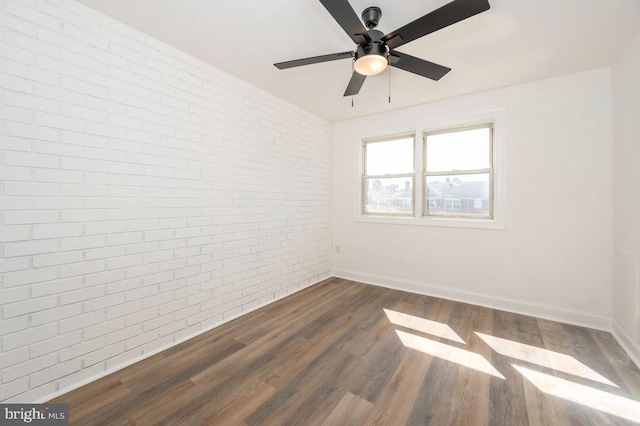 unfurnished room with brick wall, ceiling fan, dark wood finished floors, and baseboards