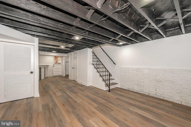 finished below grade area with wood finished floors, stairway, and brick wall
