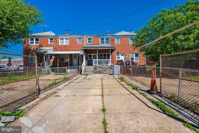 back of property with covered porch, brick siding, a fenced front yard, a chimney, and central AC unit