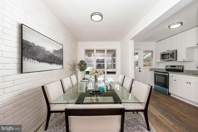 dining room featuring dark wood-style flooring and brick wall