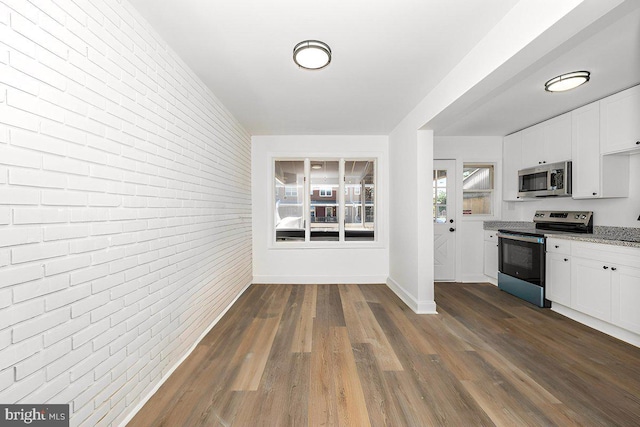 kitchen with appliances with stainless steel finishes, brick wall, white cabinetry, light stone counters, and dark wood finished floors