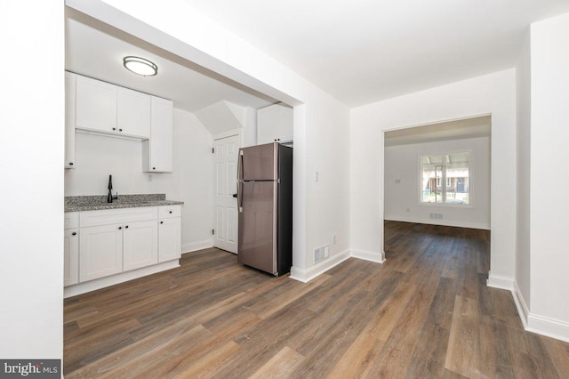 kitchen with freestanding refrigerator, white cabinetry, light stone counters, and dark wood-type flooring