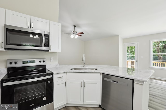 kitchen featuring appliances with stainless steel finishes, a sink, a peninsula, a ceiling fan, and light stone countertops