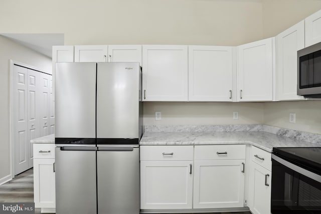 kitchen featuring appliances with stainless steel finishes, white cabinetry, light stone countertops, and light wood-type flooring
