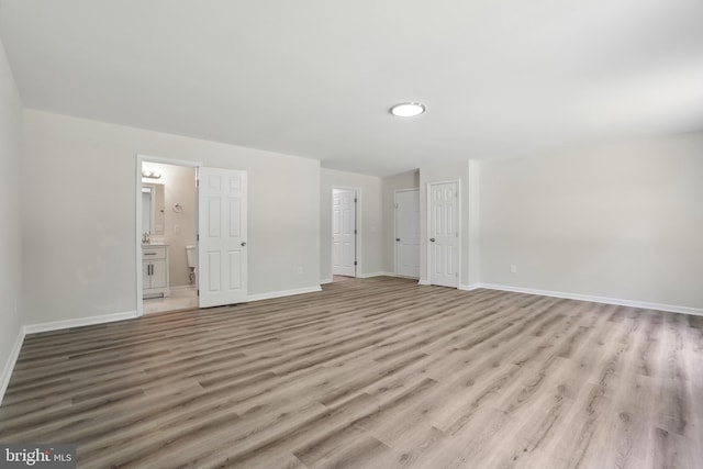 unfurnished bedroom with light wood-style floors, baseboards, and ensuite bath