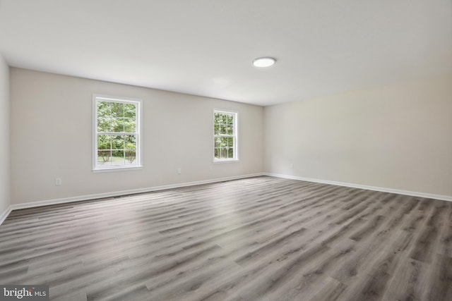 empty room with healthy amount of natural light, wood finished floors, and baseboards