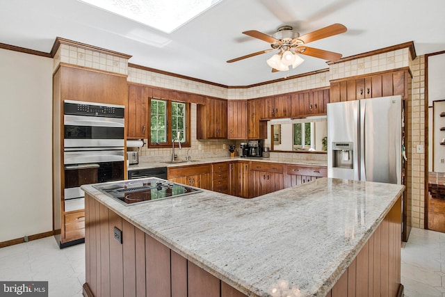 1021 Carson Dr, Huntingtown, MD 20639 - kitchen featuring appliances with stainless steel finishes, brown cabinetry, ceiling fan, backsplash, and crown molding