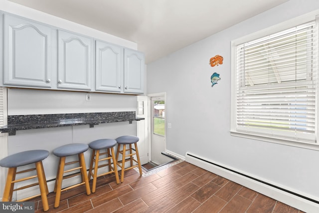 5911 Cecil Ave, Baltimore, MD 21207 - kitchen with a baseboard heating unit, a kitchen bar, dark wood finished floors, baseboards, and dark stone countertops
