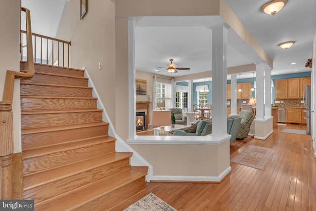 8139 Showcase Ct, Pasadena, MD 21122 - staircase featuring a ceiling fan, a glass covered fireplace, hardwood / wood-style flooring, baseboards, and ornate columns