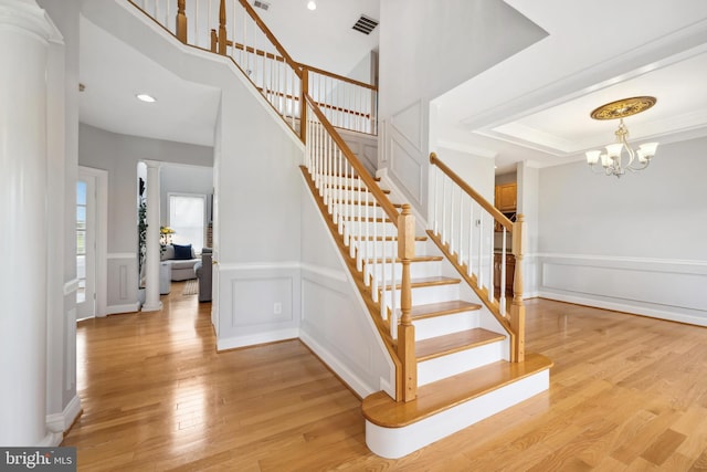 301 Nottingham Ln, Queenstown, MD 21658 - staircase with wood finished floors, a chandelier, wainscoting, a decorative wall, and decorative columns