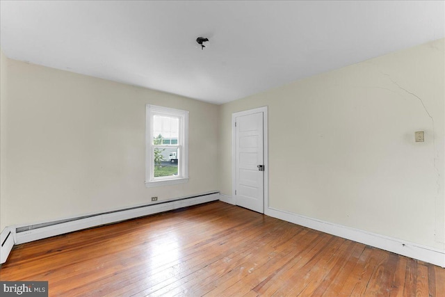 spare room featuring hardwood / wood-style floors, a baseboard heating unit, and baseboards