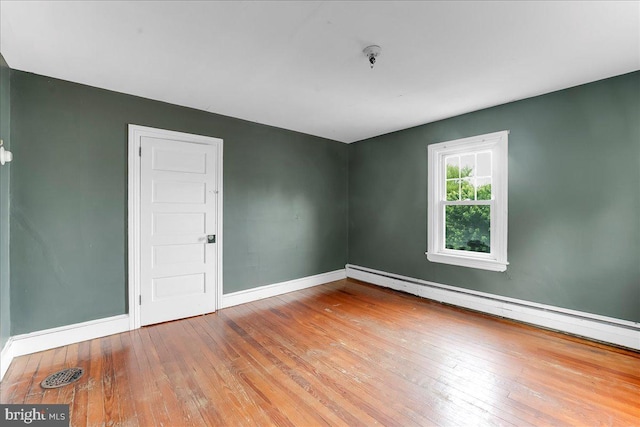 spare room featuring baseboard heating, wood-type flooring, and baseboards