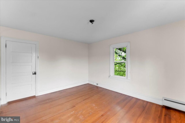 unfurnished room with baseboard heating, baseboards, and wood finished floors