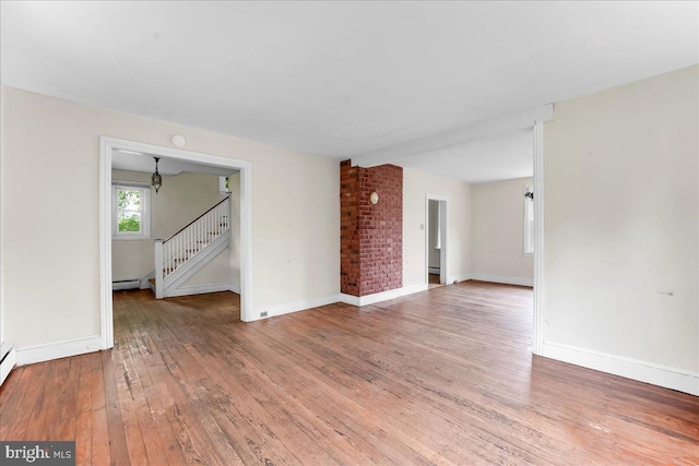 empty room featuring wood-type flooring, stairs, baseboards, baseboard heating, and a chandelier