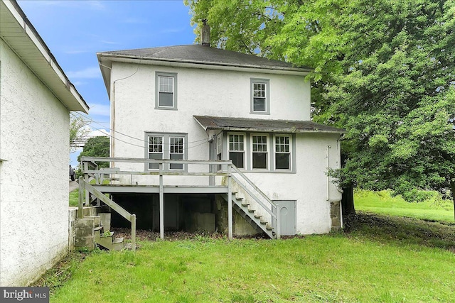 rear view of house featuring stairway, stucco siding, a wooden deck, and a lawn
