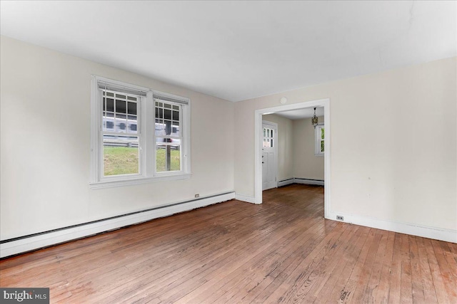 spare room featuring a baseboard heating unit, wood-type flooring, plenty of natural light, and baseboards