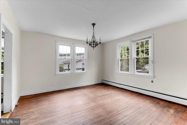 spare room featuring a baseboard heating unit, a chandelier, plenty of natural light, and hardwood / wood-style floors