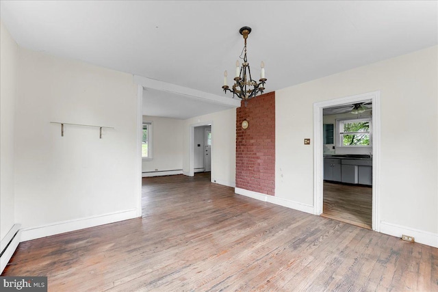 spare room featuring wood finished floors, plenty of natural light, a chandelier, and baseboards
