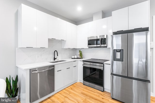 kitchen featuring stainless steel appliances, a sink, light countertops, tasteful backsplash, and light wood finished floors