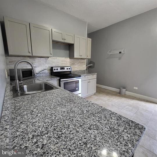 kitchen featuring stainless steel electric stove, a sink, backsplash, baseboards, and stone counters