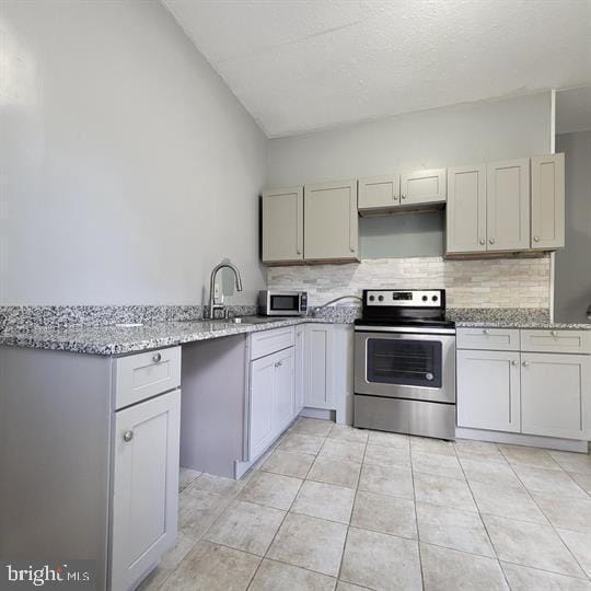 kitchen with appliances with stainless steel finishes, a sink, tasteful backsplash, light tile patterned flooring, and light stone counters
