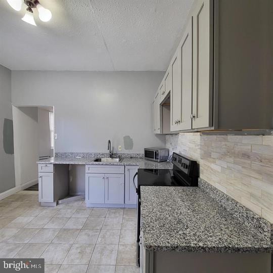 kitchen with a sink, black range with electric stovetop, light stone countertops, backsplash, and stainless steel microwave