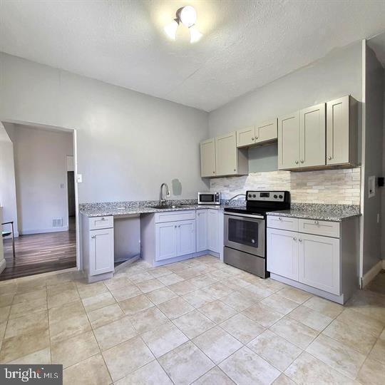 kitchen featuring appliances with stainless steel finishes, a sink, tasteful backsplash, light stone counters, and a textured ceiling