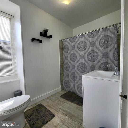 full bath featuring toilet, baseboards, vanity, and a shower with shower curtain