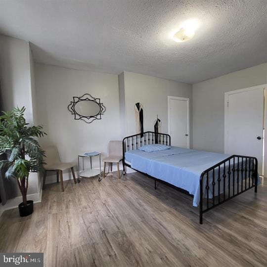 bedroom with wood finished floors, a textured ceiling, and baseboards