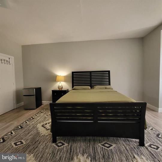 bedroom featuring freestanding refrigerator, wood finished floors, and baseboards