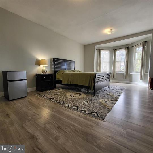 bedroom featuring freestanding refrigerator, baseboards, and wood finished floors