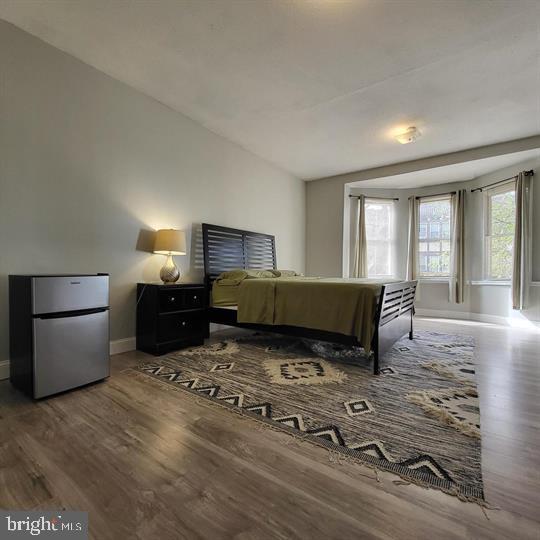 bedroom featuring freestanding refrigerator, baseboards, and wood finished floors