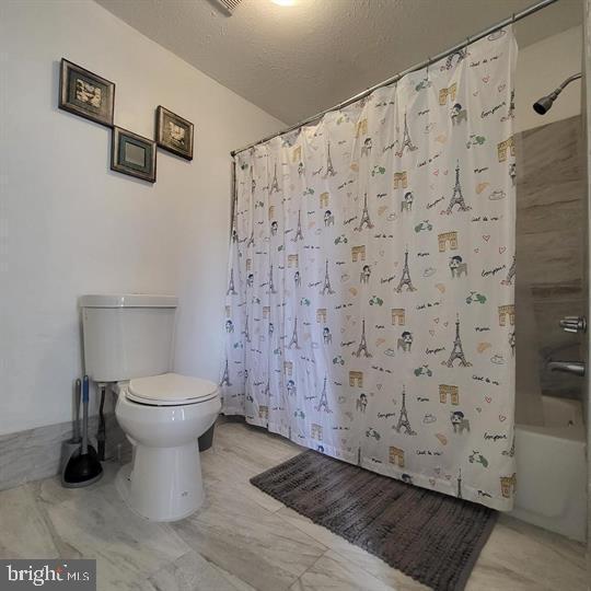 bathroom with toilet, shower / bath combo with shower curtain, marble finish flooring, and a textured ceiling