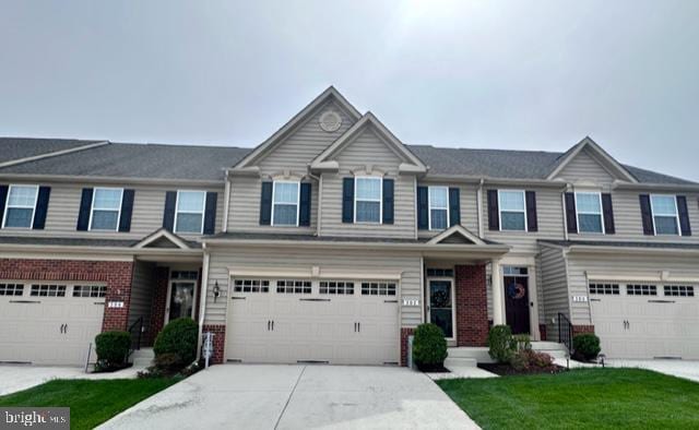 view of property with brick siding, an attached garage, driveway, and a front lawn