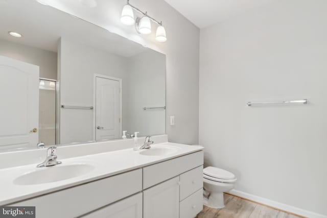 full bath with toilet, wood finished floors, double vanity, and baseboards