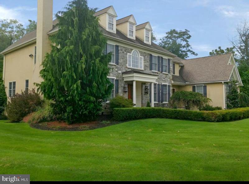 colonial house with stone siding, a chimney, a front yard, and stucco siding