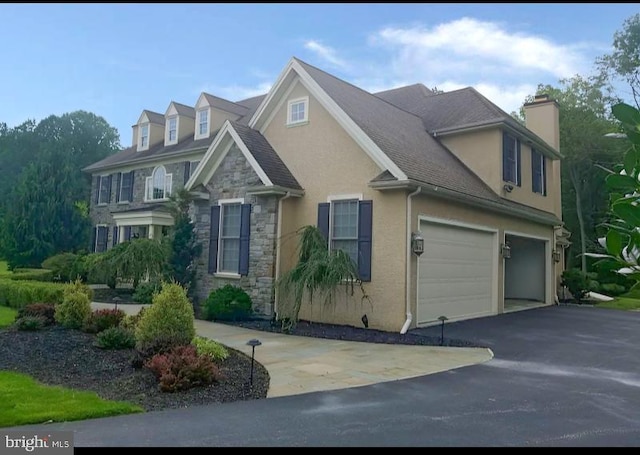 view of front of house featuring stone siding, asphalt driveway, stucco siding, a chimney, and a garage