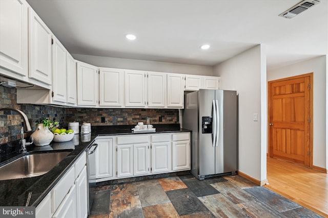 kitchen with appliances with stainless steel finishes, a sink, tasteful backsplash, dark countertops, and white cabinetry