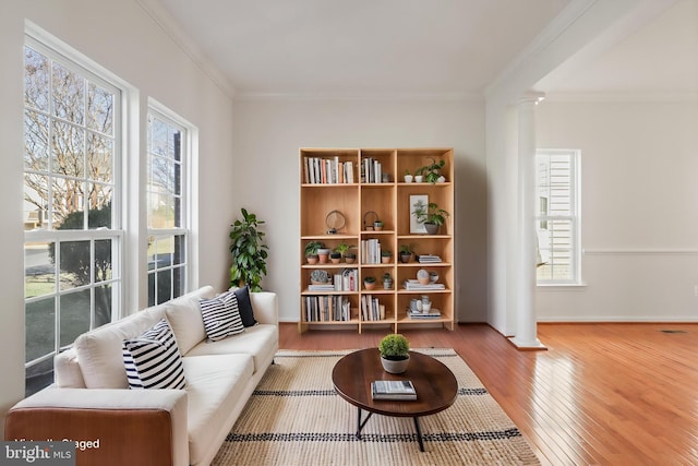 living area with ornate columns, healthy amount of natural light, ornamental molding, and wood finished floors