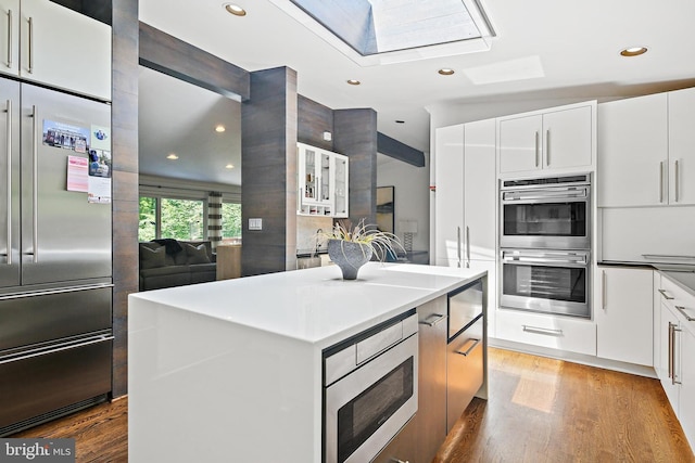 3503 Arborwood Ct, Baltimore, MD 21208 - kitchen featuring built in appliances, a skylight, light wood-style floors, a kitchen island, and white cabinets