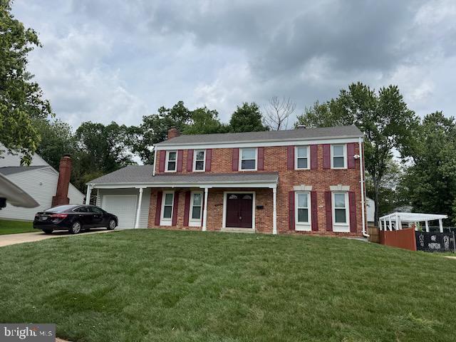 colonial house with an attached garage, a front yard, and brick siding