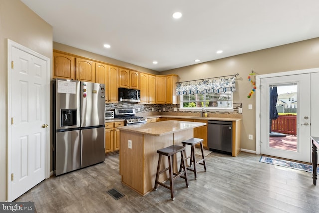 7 Otto Way, Fredericksburg, VA 22406 - kitchen with stainless steel appliances, a kitchen island, light wood-style flooring, decorative backsplash, and a breakfast bar