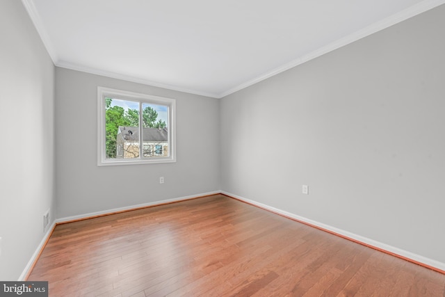 empty room with wood finished floors, baseboards, and ornamental molding