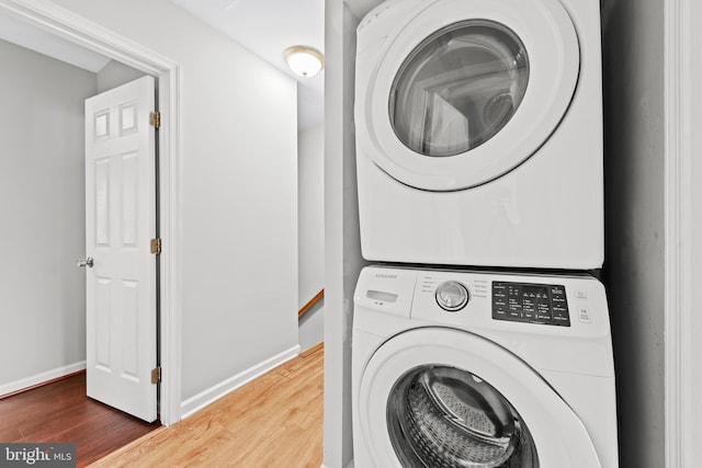 clothes washing area with stacked washing machine and dryer, wood finished floors, and baseboards