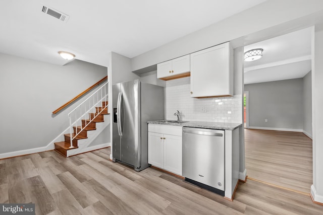 kitchen with appliances with stainless steel finishes, a sink, light stone counters, and light wood finished floors