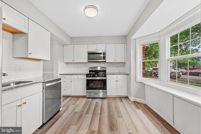 kitchen with stainless steel appliances, light wood finished floors, a sink, white cabinetry, and backsplash