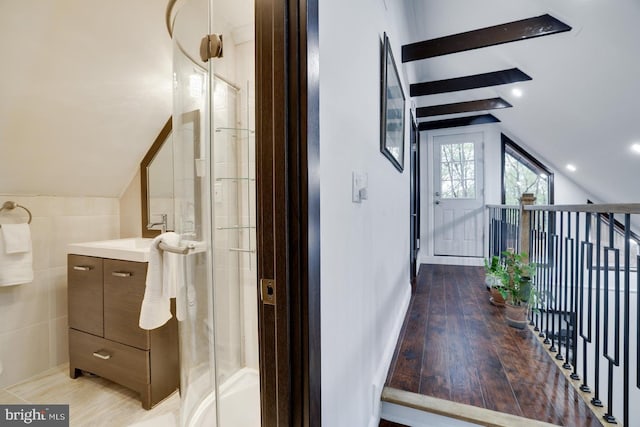 corridor with vaulted ceiling, tile walls, and light wood finished floors