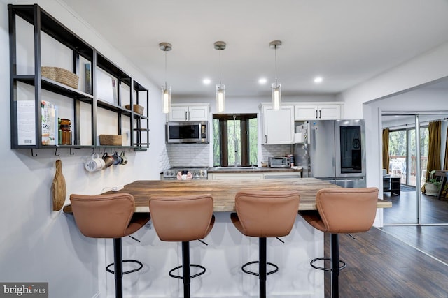 kitchen with appliances with stainless steel finishes, a kitchen breakfast bar, tasteful backsplash, white cabinets, and decorative light fixtures