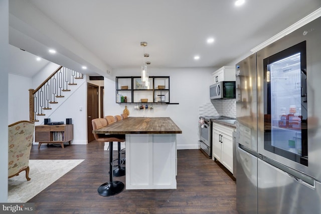 kitchen with appliances with stainless steel finishes, butcher block countertops, a kitchen breakfast bar, white cabinets, and backsplash