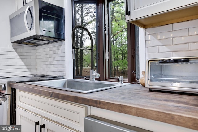kitchen featuring stainless steel microwave, a sink, decorative backsplash, and white cabinets